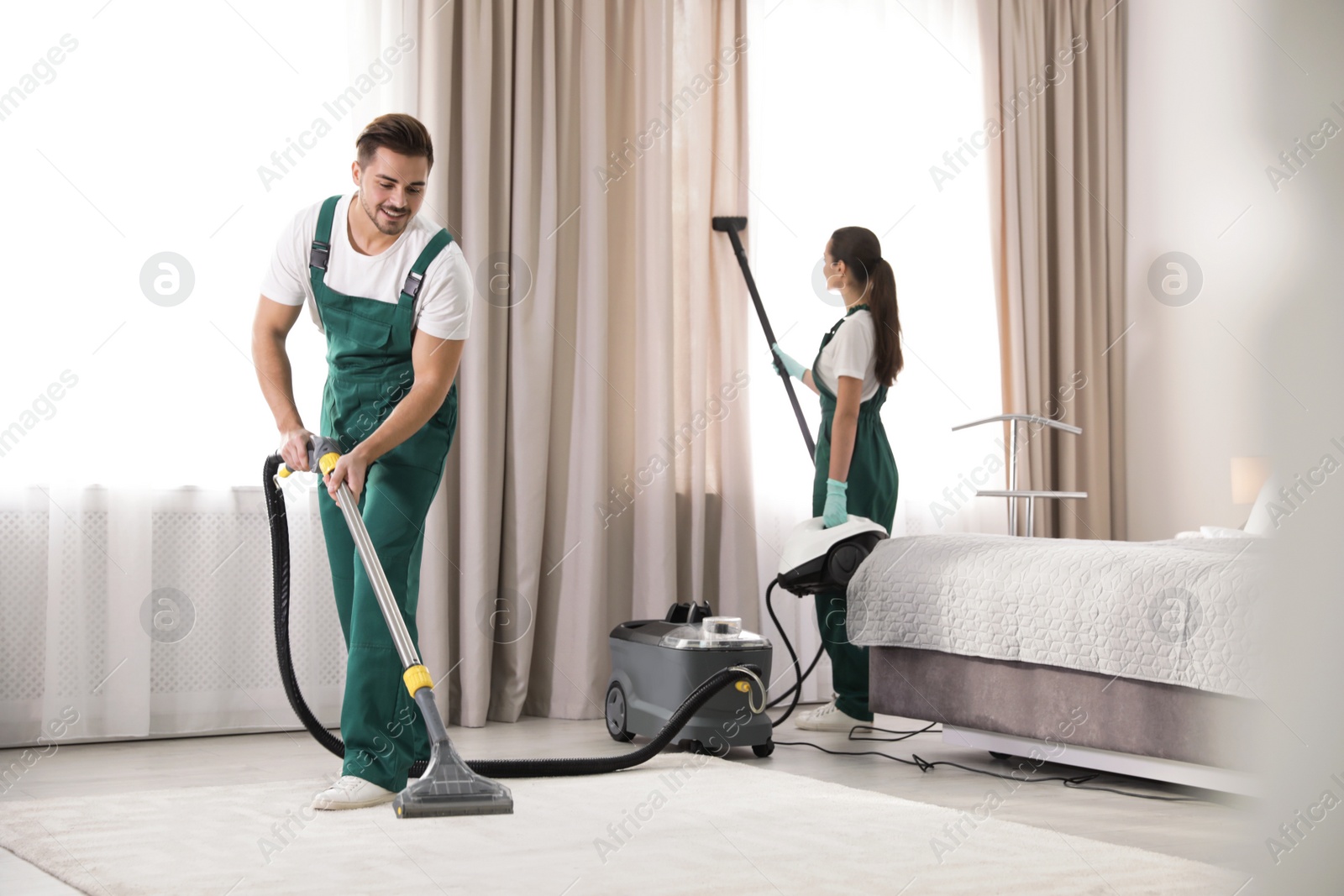 Photo of Team of janitors cleaning bedroom with professional equipment