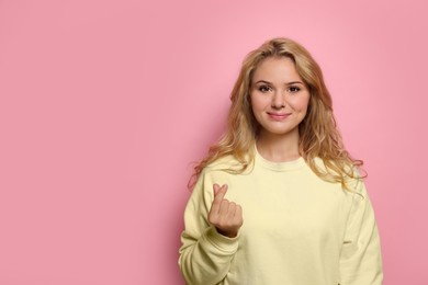 Photo of Happy young woman showing heart gesture on pink background. Space for text