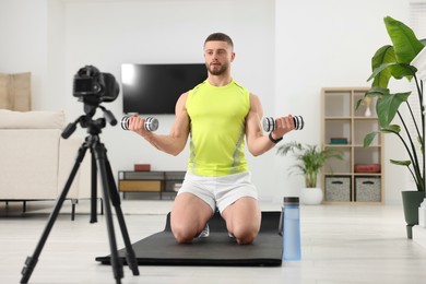 Trainer with dumbbells recording workout on camera at home