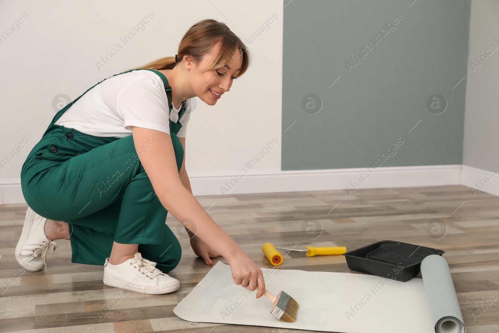 Photo of Worker applying glue onto wall paper sheet on floor indoors