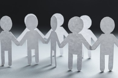 Photo of Teamwork concept. Paper figures of people holding hands on white table, closeup