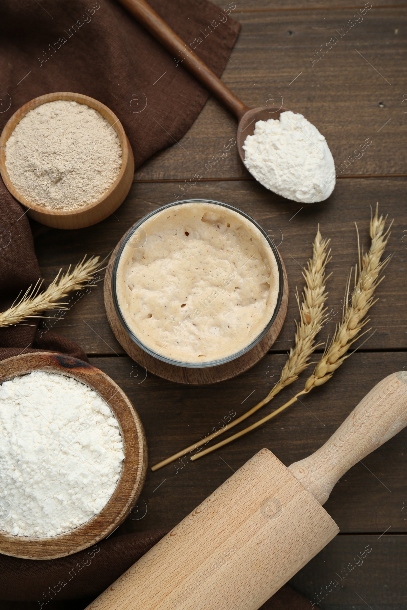 Photo of Leaven, flour, rolling pin and ears of wheat on wooden table, flat lay