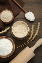 Leaven, flour, rolling pin and ears of wheat on wooden table, flat lay
