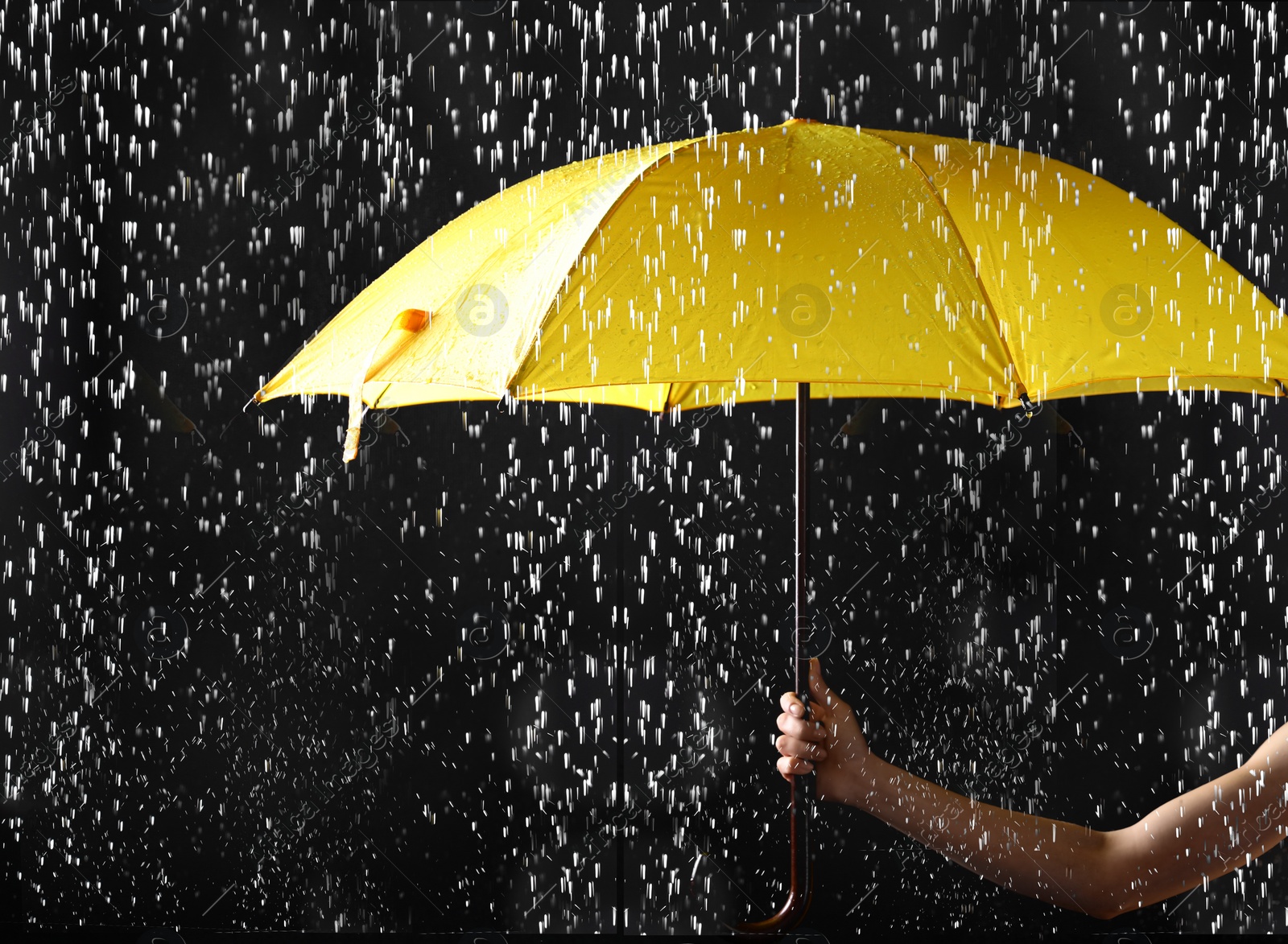 Photo of Woman holding bright umbrella under rain on dark background, closeup