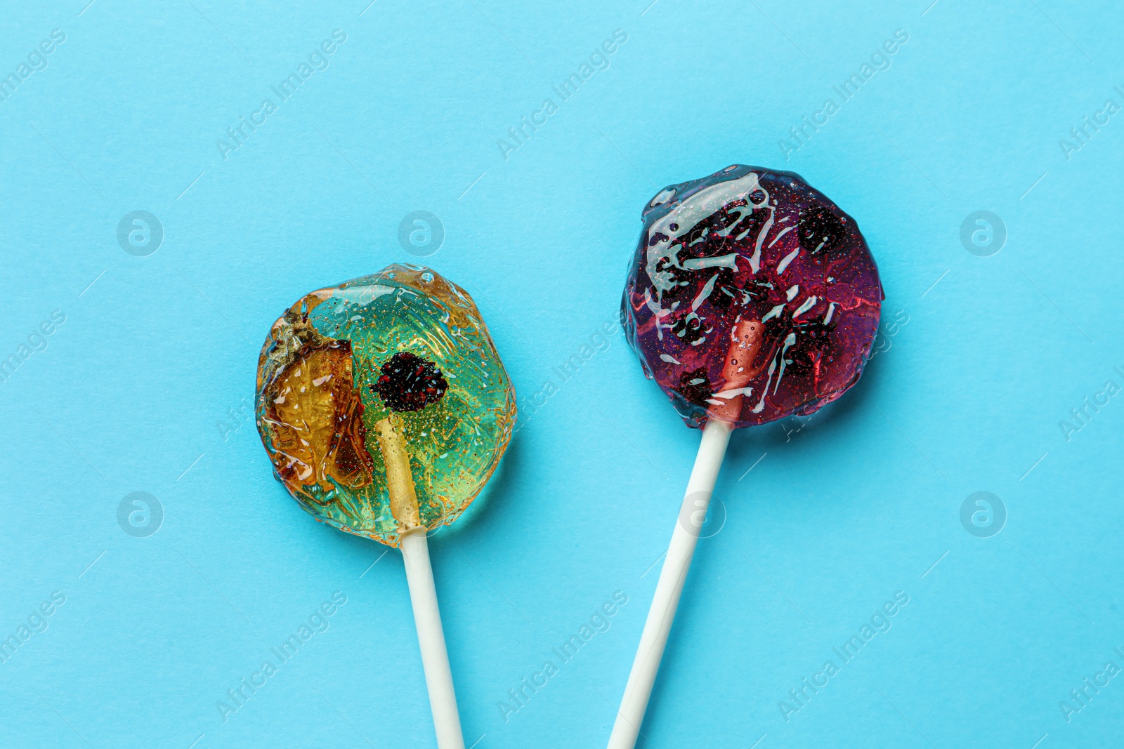 Photo of Sweet colorful lollipops with berries on light blue background, flat lay