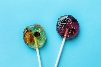 Sweet colorful lollipops with berries on light blue background, flat lay