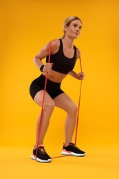 Photo of Woman exercising with elastic resistance band on orange background, low angle view