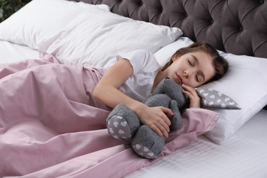 Beautiful little girl with toy rabbit sleeping in bed