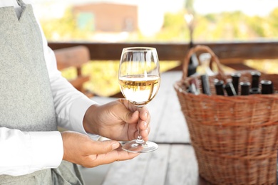 Photo of Waiter holding glass of white wine in outdoor cafe, closeup