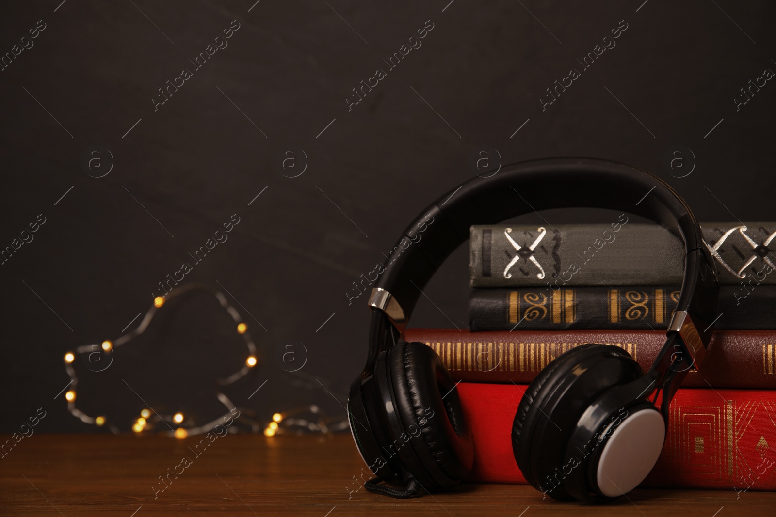 Photo of Books and headphones on wooden table against black background. Space for text