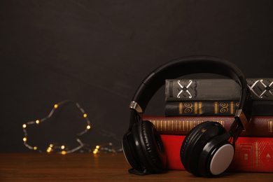 Photo of Books and headphones on wooden table against black background. Space for text