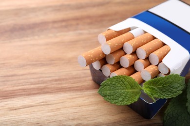 Photo of Pack of menthol cigarettes and mint leaves on wooden table, closeup. Space for text