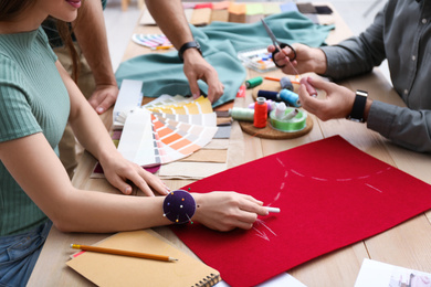 Photo of Fashion designers creating new clothes at table in studio, closeup