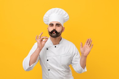 Professional chef with funny artificial moustache showing perfect sign on yellow background