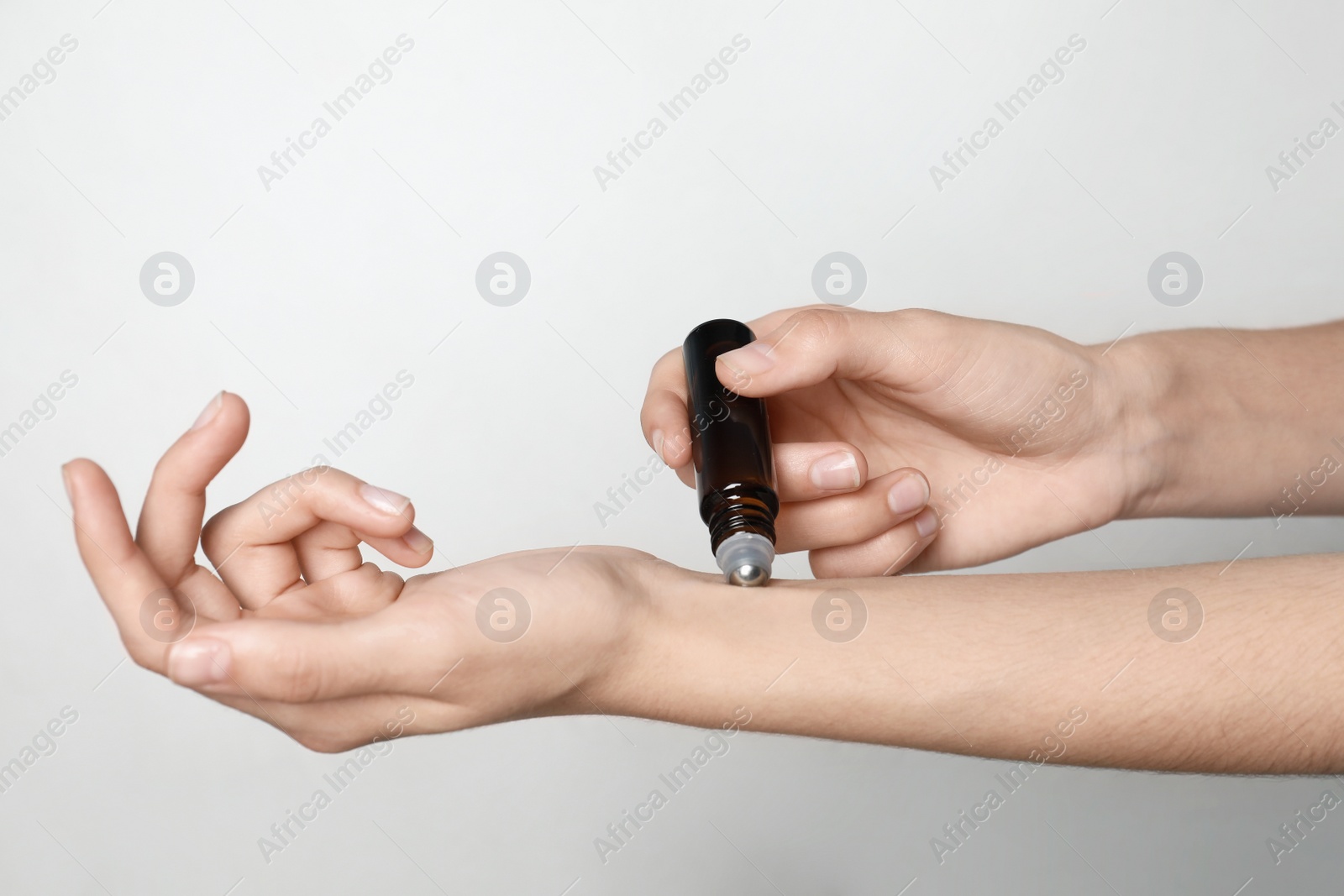 Photo of Woman applying essential oil on light background, closeup