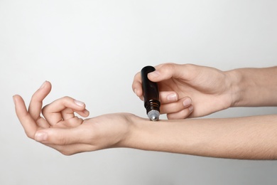 Woman applying essential oil on light background, closeup