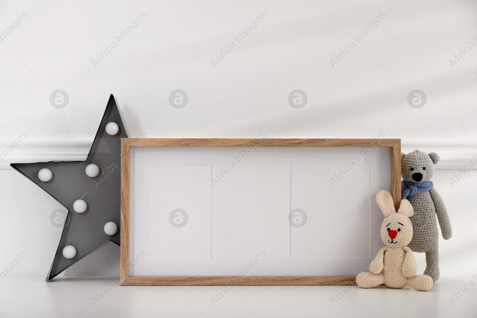 Photo of Empty photo frame, cute toys and decor near wall, space for text. Baby room interior element