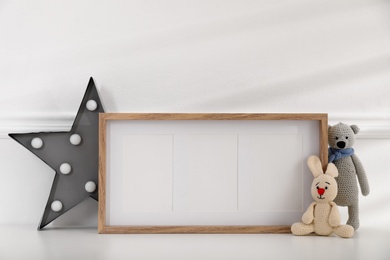 Empty photo frame, cute toys and decor near wall, space for text. Baby room interior element