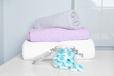 Photo of Jar with water softener tablets near stacked towels on white table