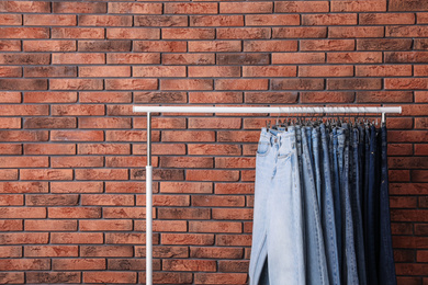 Photo of Rack with stylish jeans near brick wall