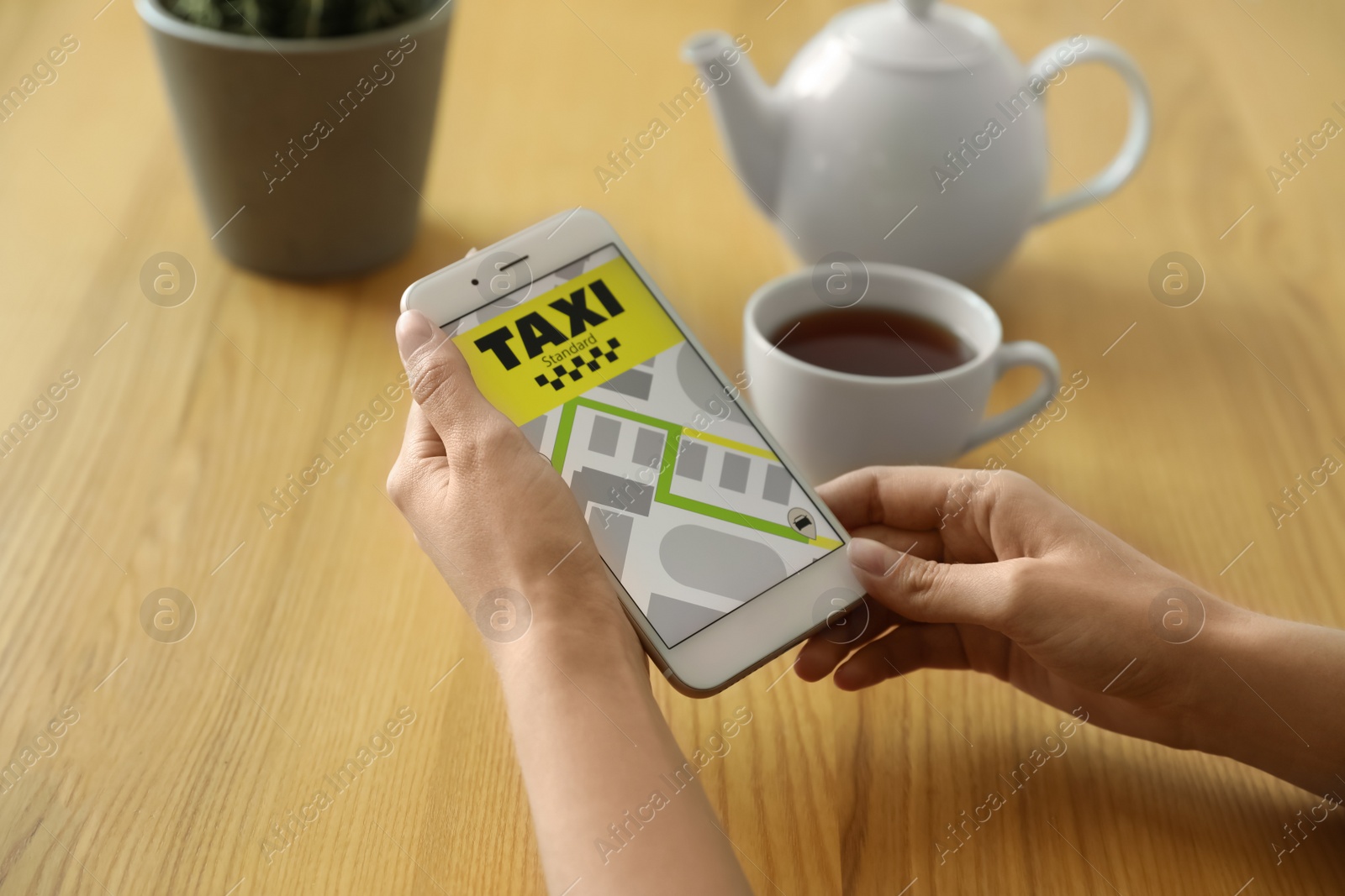 Photo of Woman ordering taxi with smartphone at wooden table, closeup