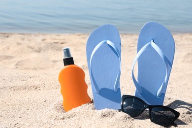 Photo of Stylish flip flops, sunglasses and sun protection spray on sandy beach