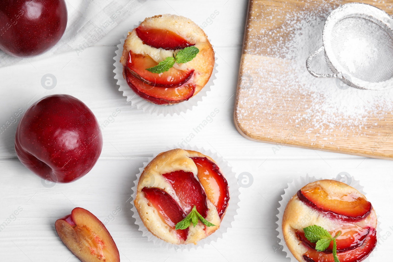 Photo of Delicious cupcakes with plums on white wooden table, flat lay