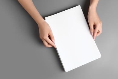 Woman holding blank paper sheets for brochure at grey table, top view. Mock up