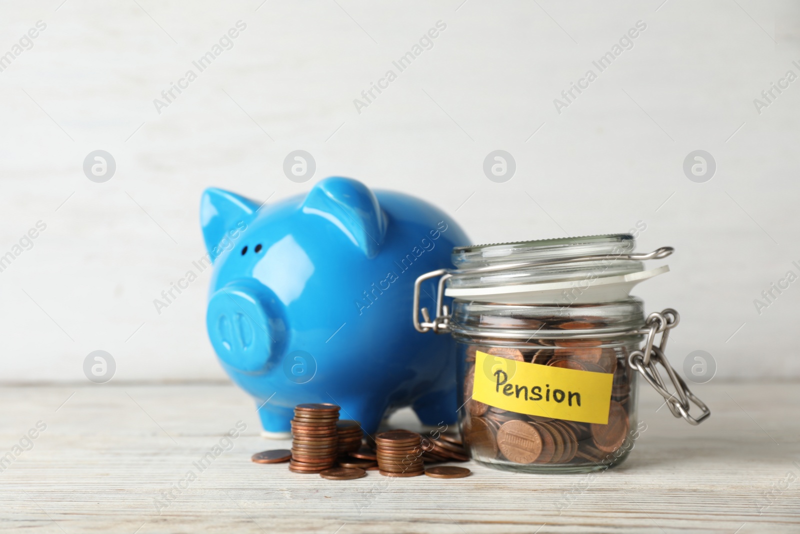 Photo of Piggy bank and jar of coins with word PENSION on table