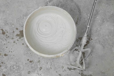 Photo of Bucket with plaster and power mixer on concrete floor, flat lay