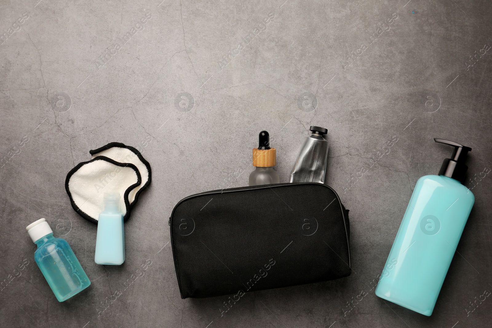 Photo of Preparation for spa. Compact toiletry bag with different cosmetic products on grey textured background, flat lay. Space for text