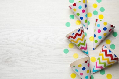 Party hats and confetti on white wooden table, space for text