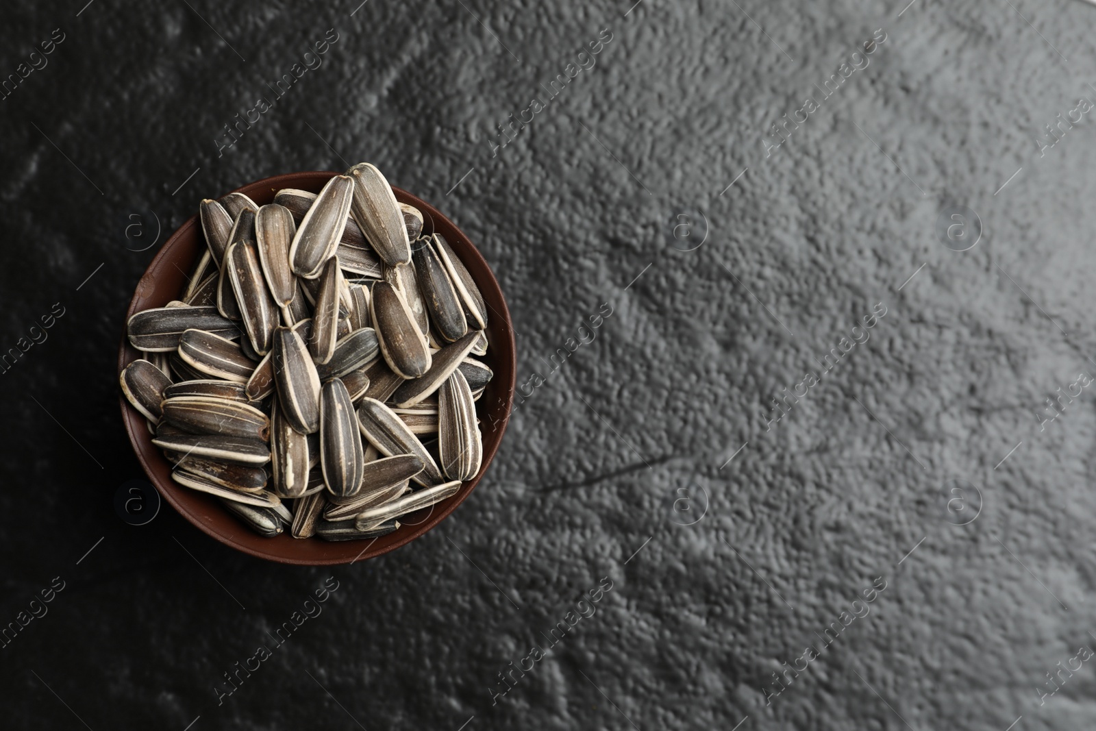 Photo of Raw sunflower seeds in bowl on black background, top view. Space for text