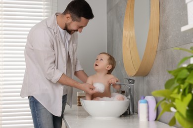 Father washing his little baby in sink at home