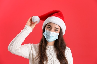 Beautiful woman wearing Santa Claus hat and medical mask on red background