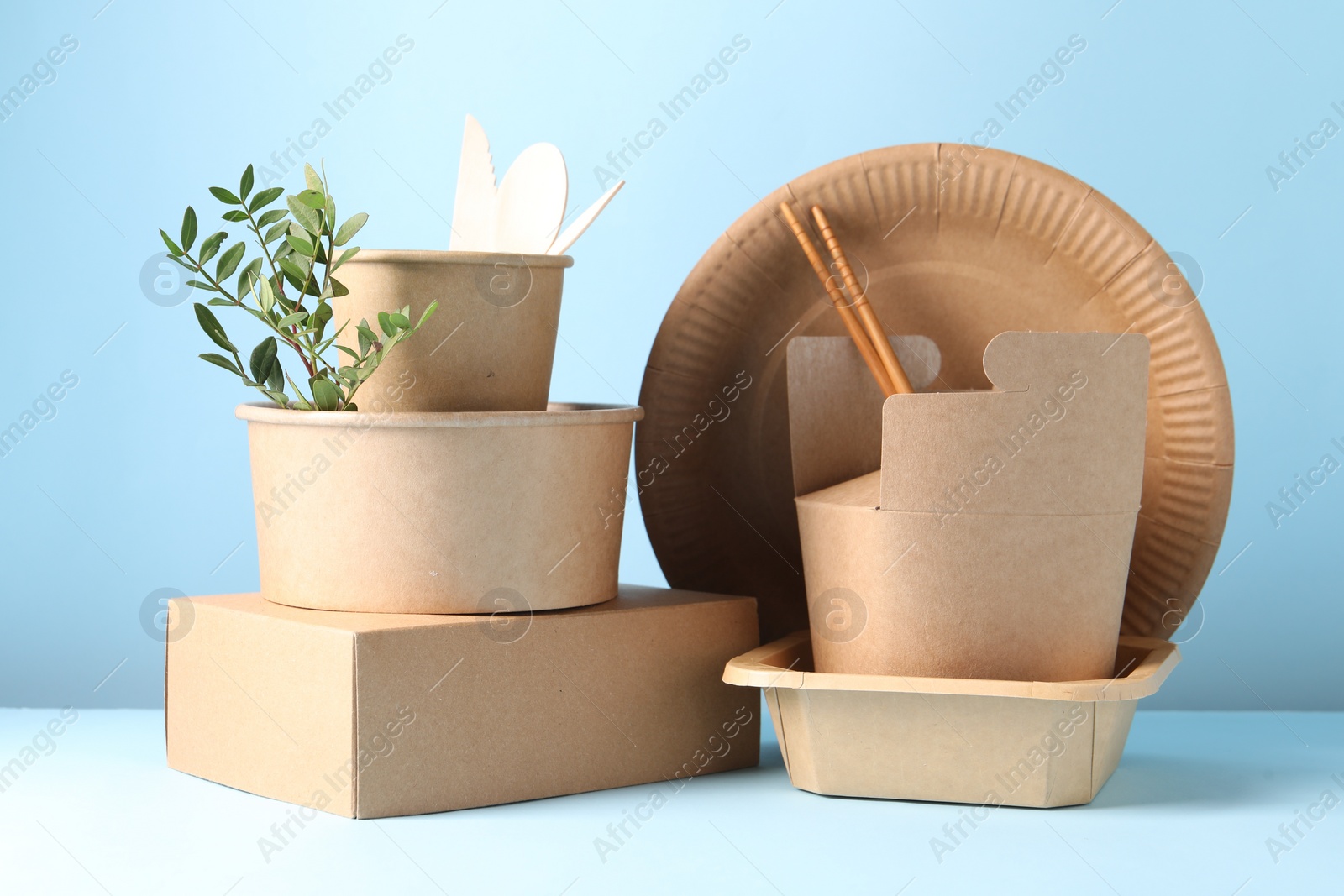 Photo of Eco friendly food packaging. Paper containers, tableware and green twig on white table against light blue background