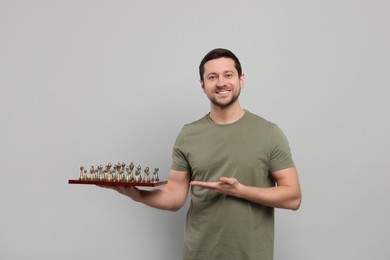 Handsome man showing chessboard with game pieces on light grey background