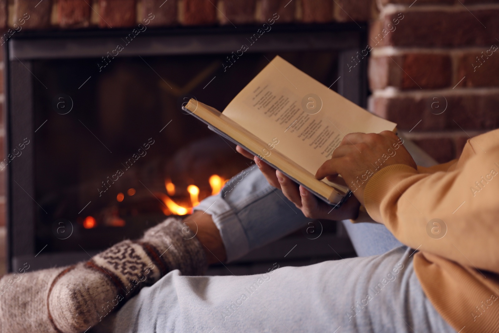 Photo of Man reading book near fireplace at home, closeup