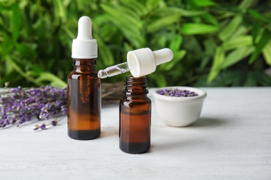 Natural herbal oil in glass bottles and lavender flowers on wooden table against blurred background