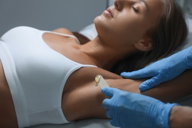 Young woman undergoing hair removal procedure of armpits with sugaring paste in salon