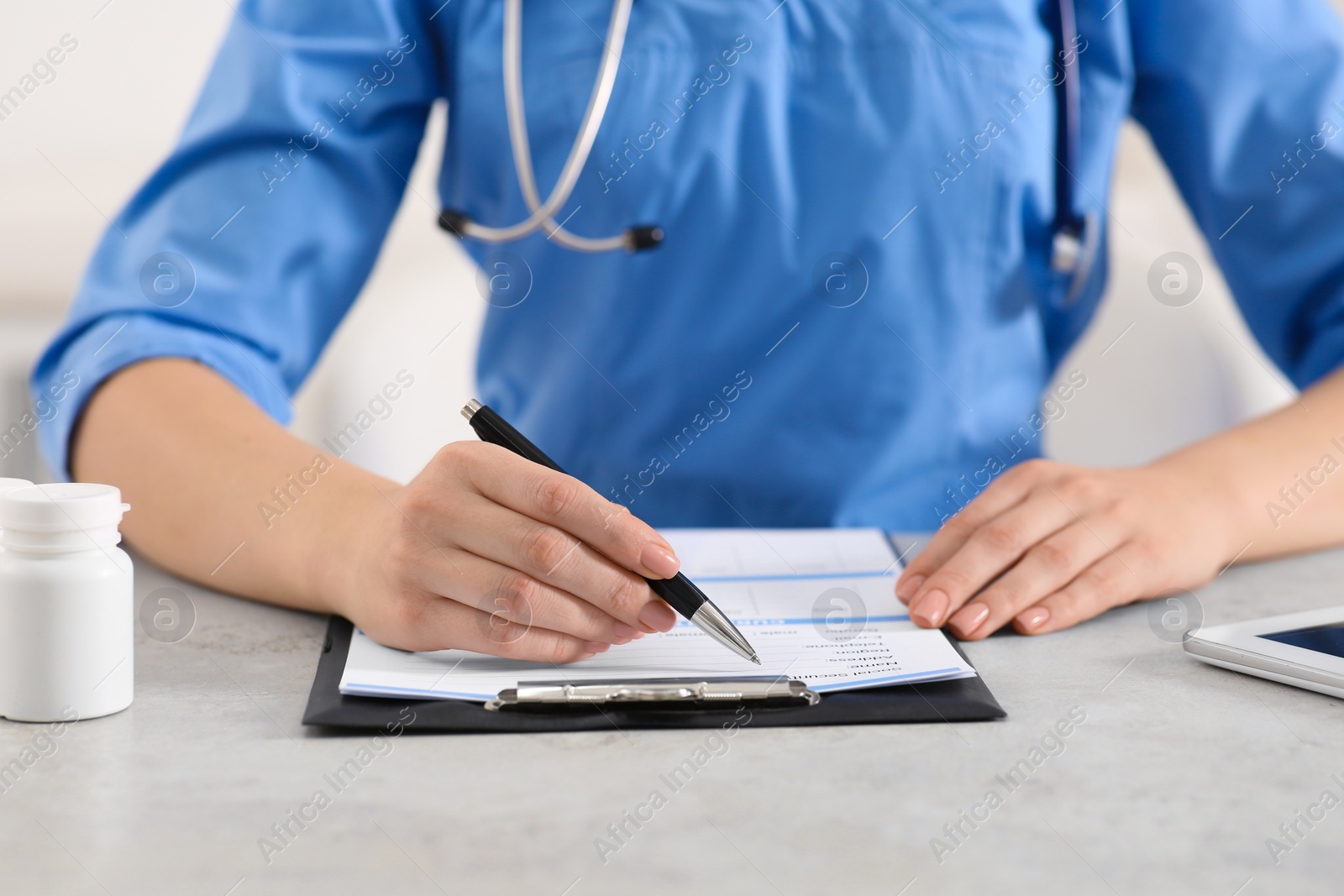 Photo of Doctor filling patient's medical card at table in clinic, closeup