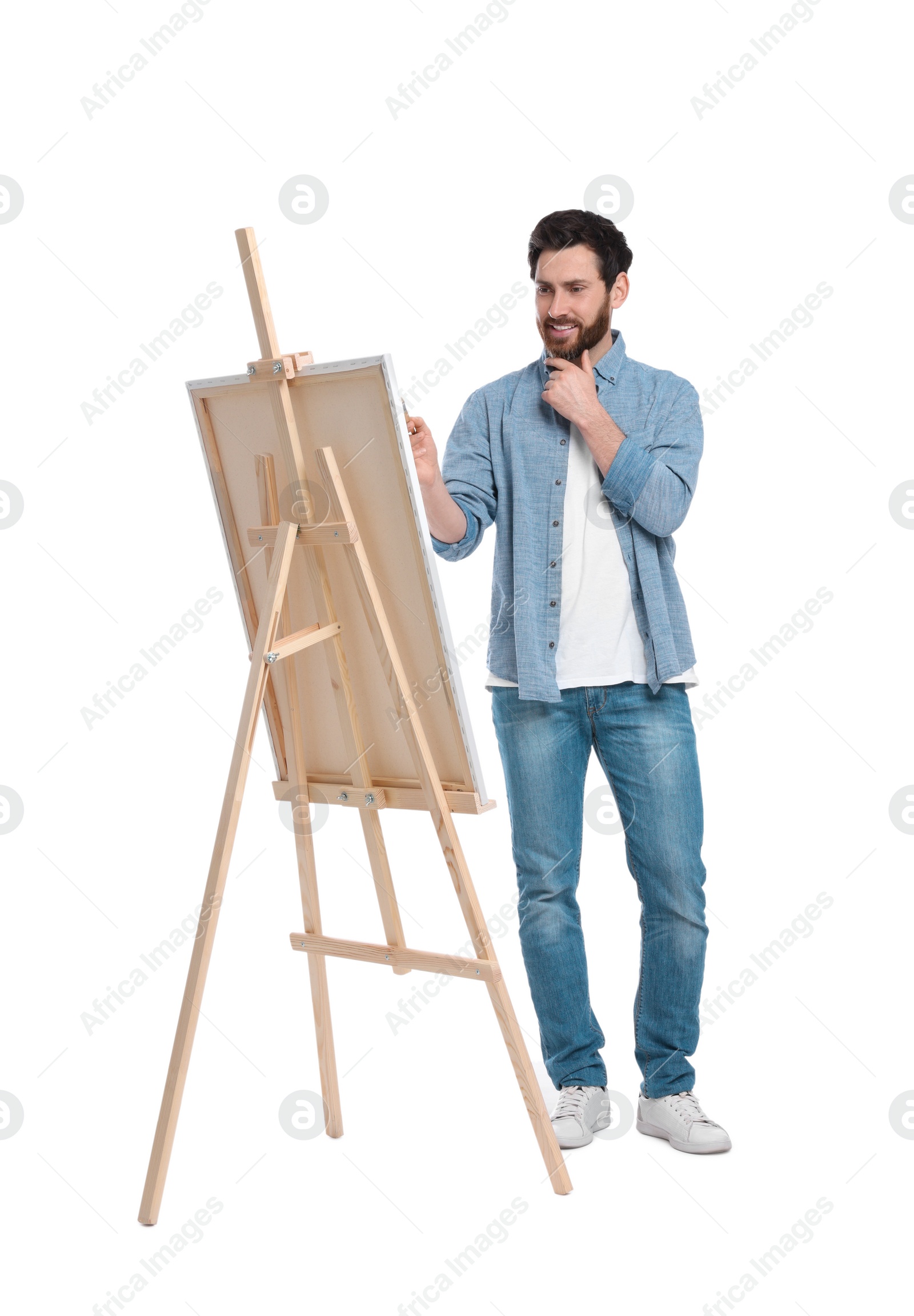 Photo of Happy man painting with brush against white background. Using easel to hold canvas