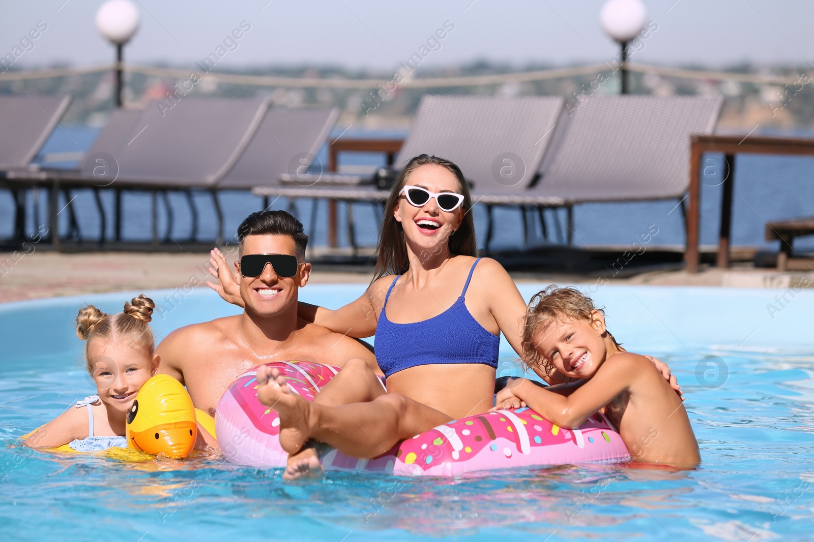 Photo of Happy family with inflatable rings in outdoor swimming pool on sunny summer day