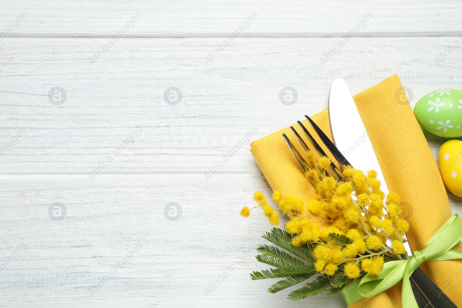 Photo of Top view of cutlery set with floral decor on white wooden table, space for text. Easter celebration