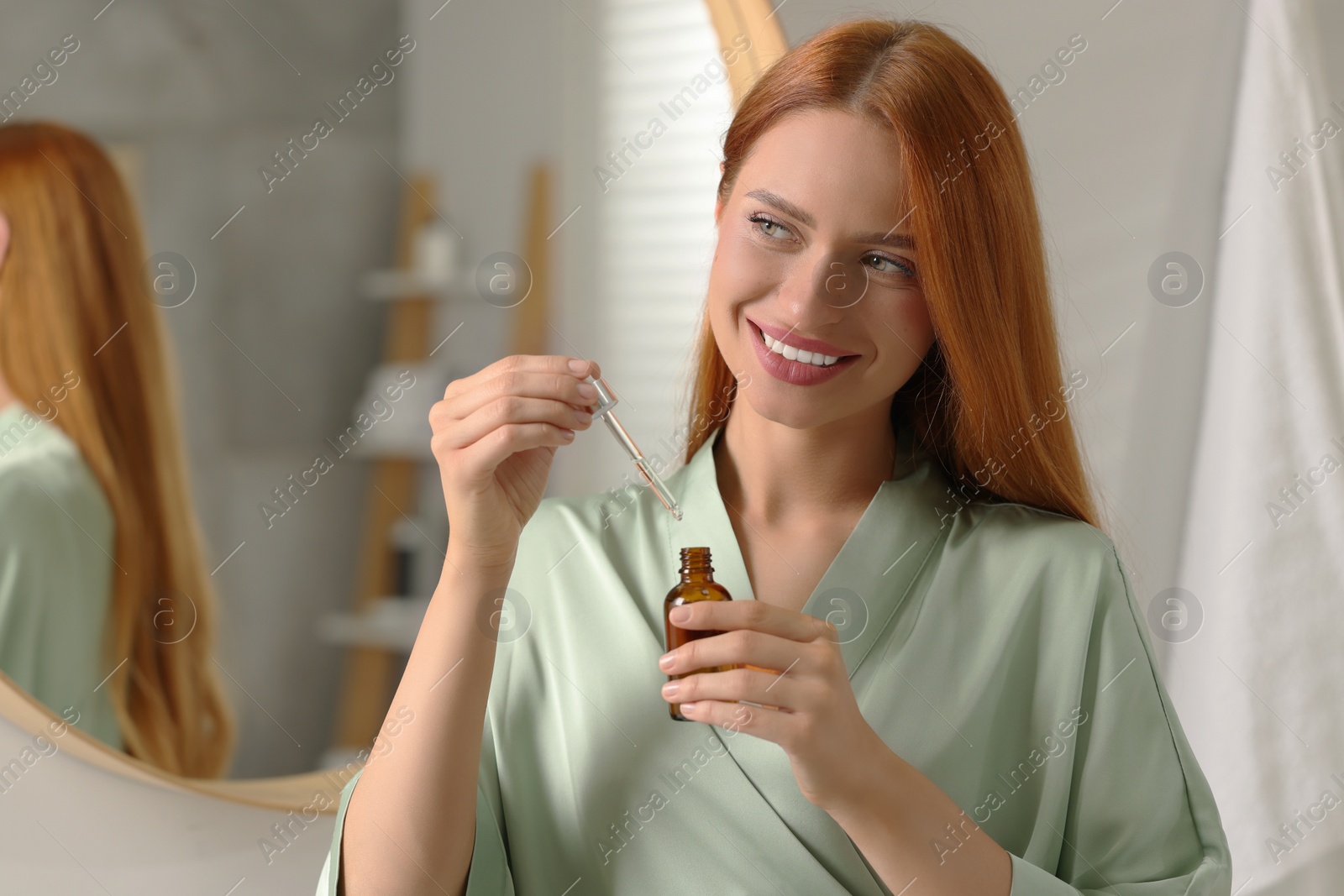 Photo of Beautiful young woman with bottle of cosmetic serum in bathroom, space for text