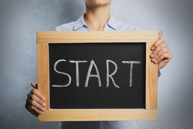 Photo of Woman holding blackboard with word Start on light background, closeup