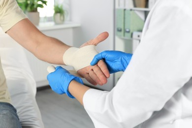 Doctor applying medical bandage onto patient's hand in hospital, closeup