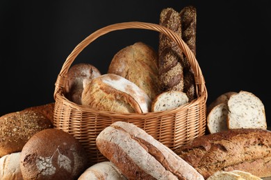 Photo of Wicker basket with different types of fresh bread against black background