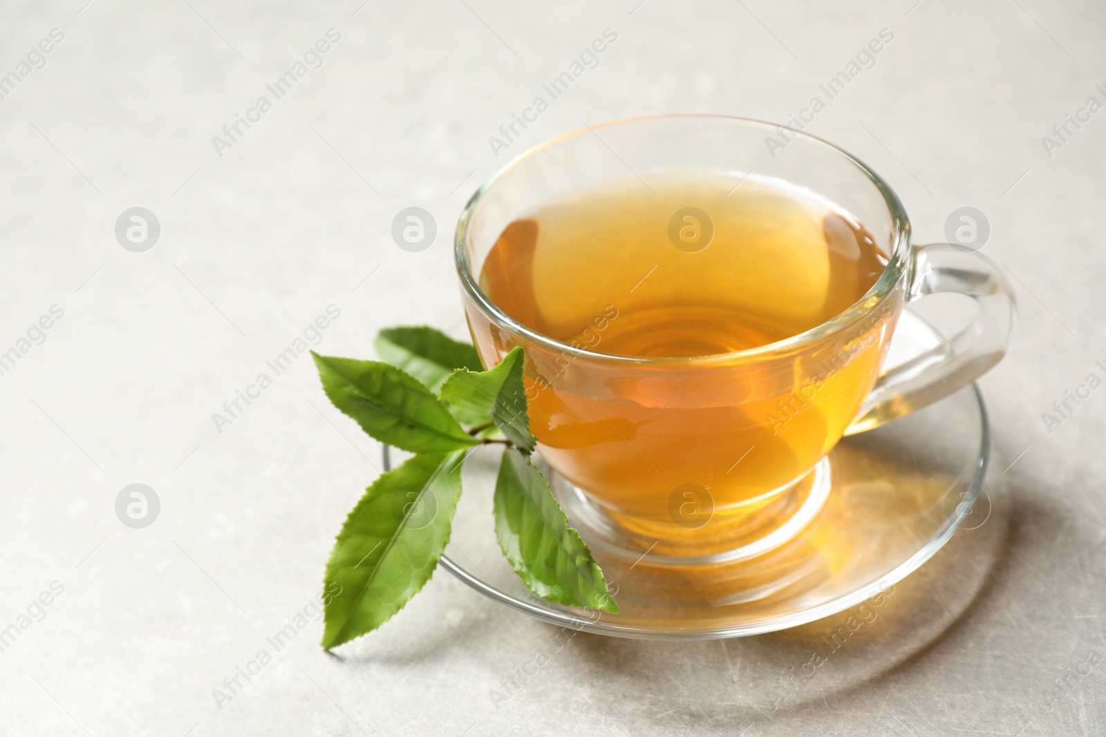 Photo of Cup of green tea and leaves on grey table