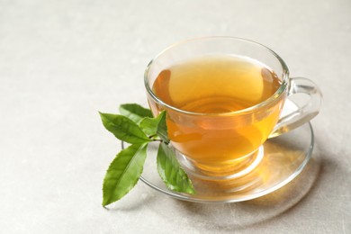 Cup of green tea and leaves on grey table